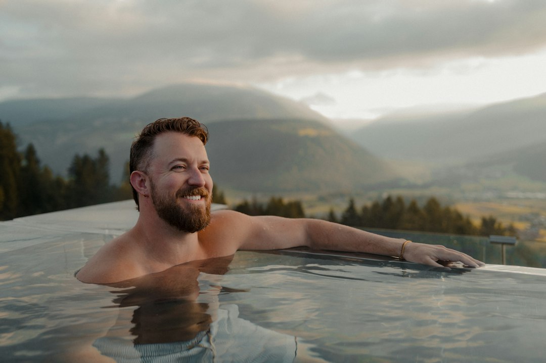 A man with a beard in an infinity pool overlooking mountains in Sorafurcia, Italy
