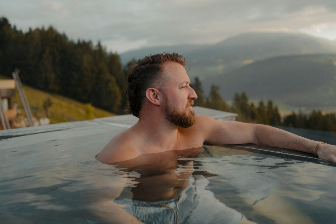 A man with a beard in an infinity pool overlooking mountains in Sorafurcia, Italy